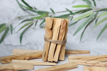 Palo santo sticks and green branch on white marble table
