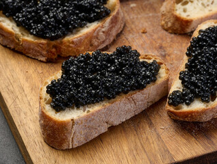 Sandwiches with black caviar served on a wooden board, top view