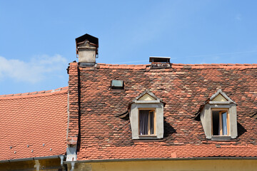 A building with a terracotta tiled roof featuring dormer windows and a chimney against a clear blue sky