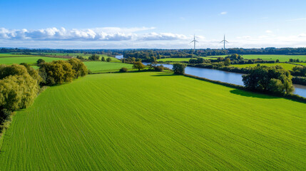 Lush green fields with wind turbines and river under clear blue sky