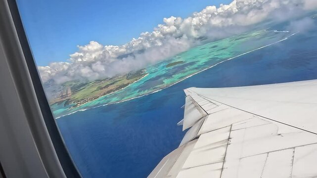 Large airplane climbing after takeoff from Mauritius airport. View from the window above the wing, showing the island, ocean, and low clouds.