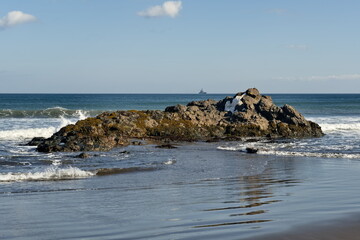 Russia. The Far East. The Kuril Islands. View of the basalt rock outcrops of volcanic origin on the sea sandy shore of Iturup island.