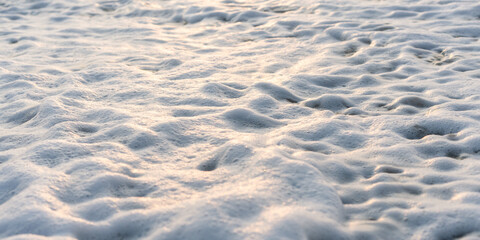 Close-up of a coral sand beach with white sea foam washing up and resting on the surface.