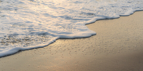 Close-up of a coral sand beach with white sea foam washing up and resting on the surface.