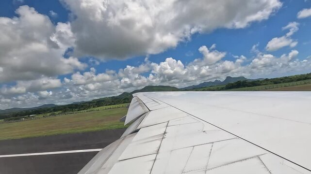 Large airplane taking off from Mauritius airport. View from the window above the wing, showing the runway and tropical landscape.