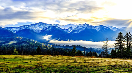 Obraz premium A mountain range covered with snow, clouds, and a forest beneath, suitable for showcasing natural beauty and adventure