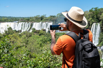 Fototapeta premium Turista de espaldas, tomando una foto a las cataratas del Iguazú, en el Parque Nacional Iguazú, Argentina