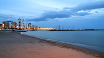 Obraz premium Peaceful beach at dusk with city skyline and marina. Tranquil scene for travel brochure or coastal promotion