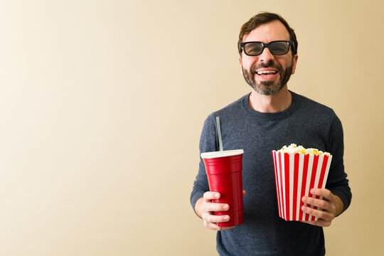 Handsome man enjoying movie with popcorn and soda, smiling at cinema