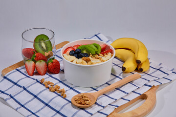 A vibrant and healthy smoothie bowl topped with fresh strawberries, blueberries, kiwi, banana slices, almonds, and pistachio. Placed on a paper cup.