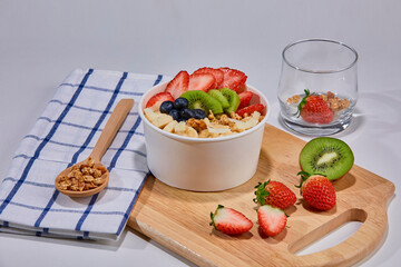 A vibrant and healthy smoothie bowl topped with fresh strawberries, blueberries, kiwi, banana slices, almonds, and pistachio. Placed on a paper cup.