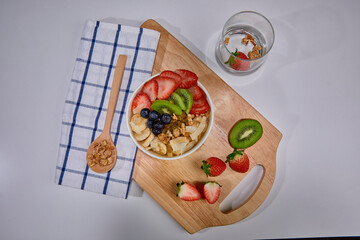 A vibrant and healthy smoothie bowl topped with fresh strawberries, blueberries, kiwi, banana slices, almonds, and pistachio. Placed on a paper cup.