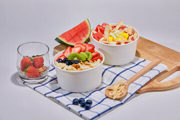 A delicious and nutritious granola bowl topped with fresh strawberries, blueberries, kiwi, banana slices, coconut flakes, and almonds. Placed on a wooden board with a checkered napkin.