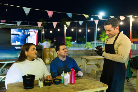 Latin couple ordering street food at night talking to a food truck worker at night