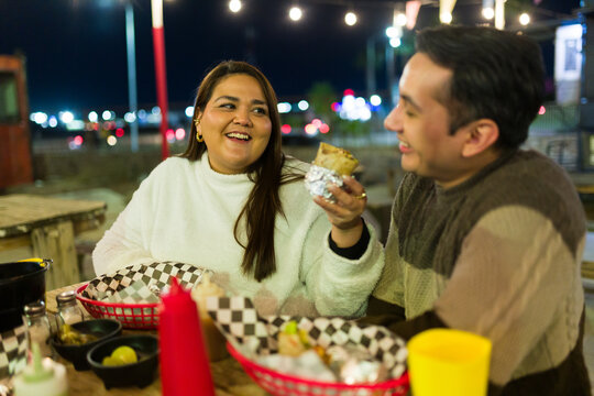 Cheerful friends sharing a meal of burritos and tacos at an outdoor food truck, enjoying the vibrant night atmosphere