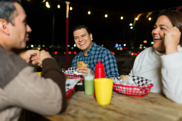 Diverse friends savoring mexican street food, laughing together near brightly lit food truck during urban evening gathering