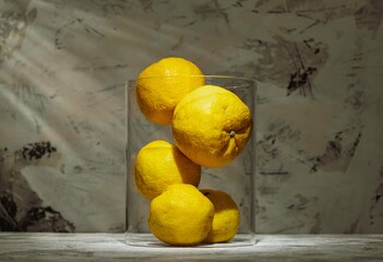 Fresh yuzu lemons fill a clear vase, their vibrant yellow hues standing out against a beautifully textured backdrop that enhances their citrus appeal