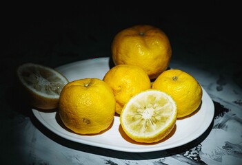 A collection of bright yellow yuzu lemons rests on a smooth plate, with one sliced open to reveal its juicy interior. This arrangement showcases their rich colors and distinct features