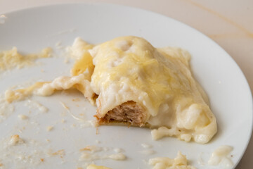 a plate of cannelloni, with bechamel sauce on top and gratin cheese on a white plate on a white veined marble table