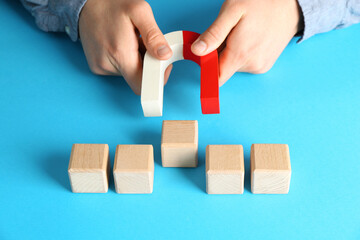Man with magnet attracting wooden cubes on light blue background, closeup