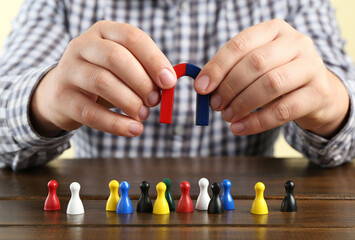 Man with magnet attracting game pieces at wooden table, closeup
