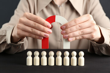 Woman with magnet attracting game pieces at wooden table, closeup