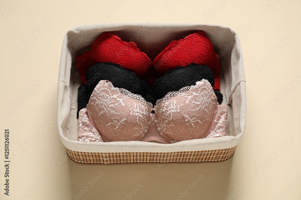 Wall mural Beautiful bras in basket on beige background, above view