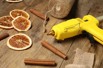 Hot glue gun and handicraft materials on wooden background, closeup