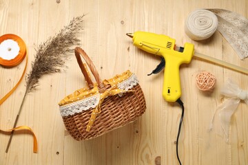 Hot glue gun and handicraft materials on wooden background, flat lay