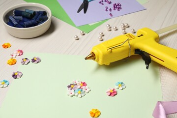 Hot glue gun and handicraft materials on wooden background, closeup