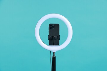 Ring lamp with smartphone on light blue background