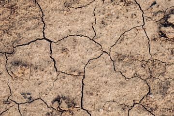 Dry cracked earth texture showing severe drought, a consequence of climate change and global warming, with deep cracks forming intricate patterns on the parched surface