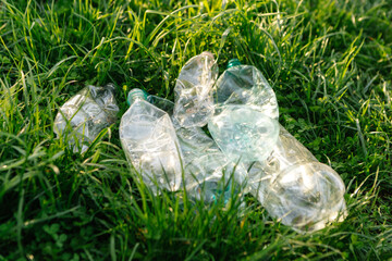 Many used crushed plastic bottles polluting a patch of green grass in nature, representing environmental damage from plastic waste and the importance of recycling and proper waste disposal. Ecology