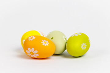 Four decorative eggs in yellow and green with floral patterns rest on a white background. Their bright colors and simple design create a clean, modern composition.