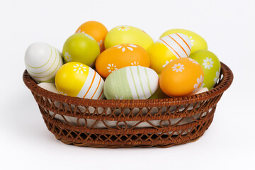 A woven basket with vibrant yellow and green hand-painted eggs featuring floral and striped patterns. The clean white background makes the colors stand out.