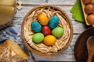 A vibrant assortment of red, blue, yellow, and green dyed eggs resting in a rustic basket, surrounded by bread, natural textiles, and raw ingredients, evoking a sense of tradition and homemade charm.