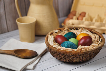 A woven basket with dyed eggs on linen rests against a rustic wooden backdrop, enhanced by soft lighting and natural textures.