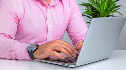 Naklejka premium A person in a pink shirt is typing on a laptop, with a green plant in the background, suggesting a modern workspace atmosphere.