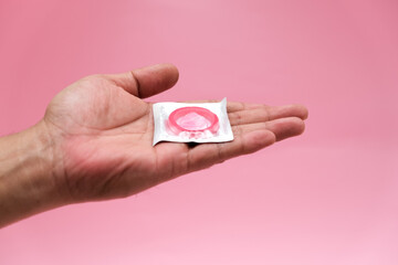 Safe sex concept. Young guy holding condom in wrapper on light pink background, copy space.