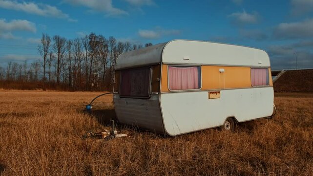 A vintage caravan sits alone in an expansive field its pastel colors contrasting with the dry brown grass Bright sunlight illuminates the scene showcasing clear skies