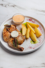 Top view of a delicious grilled chicken served with potato wedges, a creamy sauce, and herbs on a white plate, creating an enticing culinary scene. Restaurant or cafe menu, cookbook recipe
