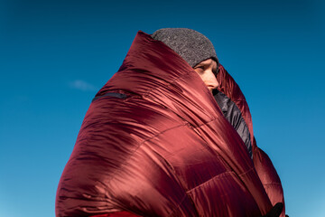 Mountain portrait of a young man in harsh light, wrapped in a sleeping bag