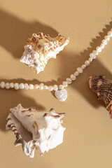 Necklace made of natural river pearls with heart pendant on beige background. Necklace and seashells