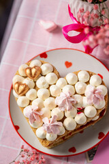 bento cake in the shape of a heart for two lovers, honey cake with buttercream and marshmallows, cake on a plate with hearts, pink gypsophila in a vase with a ribbon, light background, cake on a pink 