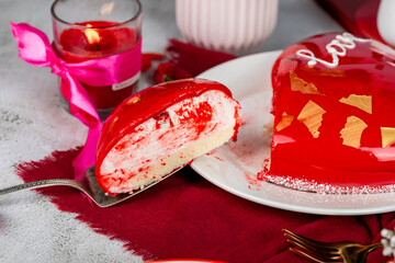 heart-shaped mousse cake in red glaze with gold decor on a white plate, red and pink carnations,...
