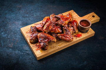 Authentical barbecue chicken wings with hot chili sauce as marinade served as close-up on a wooden design cutting board