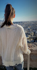 Photo of a girl standing with her back to the camera on an observation deck overlooking the city....