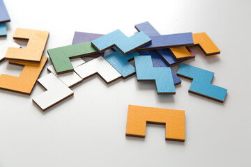Scattered colorful wooden puzzle pieces on a white background. The geometric shapes create a playful and educational composition, symbolizing logic and problem-solving