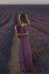 Eine Frau steht in einem Lavendelfeld bei Sonnenuntergang und h&auml;lt einen Strau&szlig;. Ihr Gesicht ist verborgen, was eine ruhige und vertr&auml;umte Atmosph&auml;re schafft.