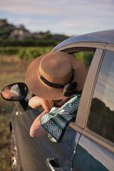 Frau in einem Hut, die aus einem Autofenster lehnt und in die Ferne blickt. Stylisches Reise- und Roadtrip-Konzept mit einem Gef&uuml;hl von Freiheit und Abenteuer.